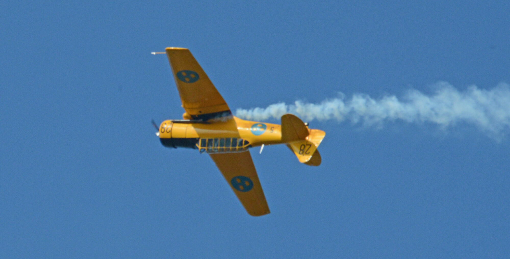 En gul SK16 uppochner i luften med blå himmel bakom